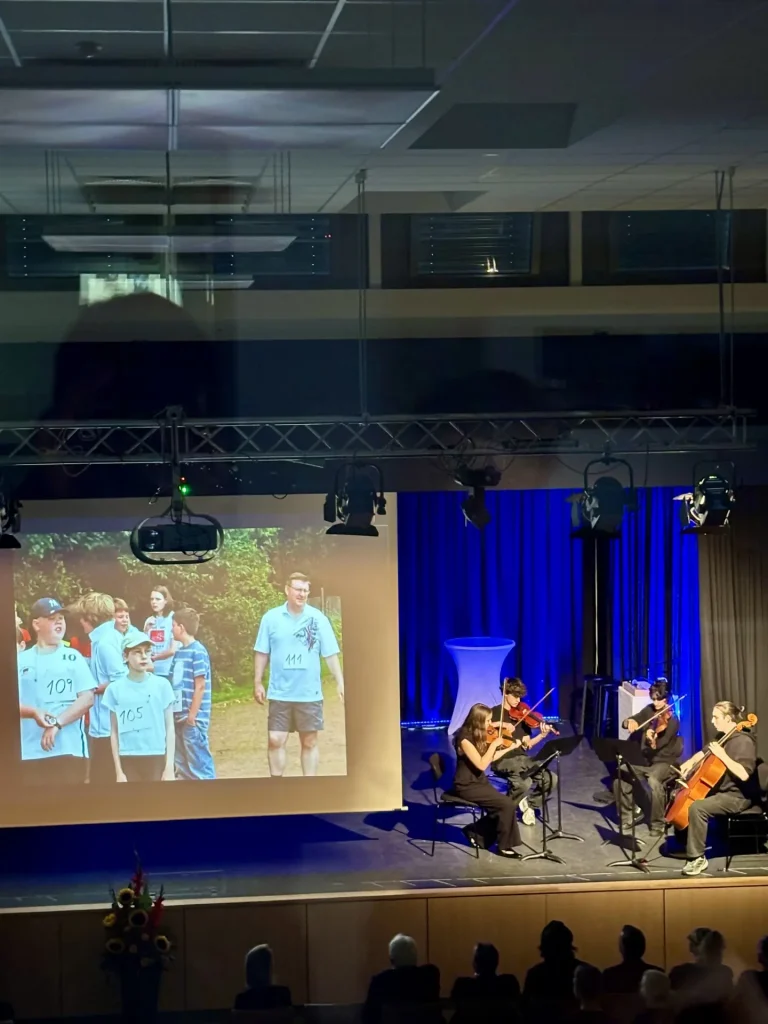 Streichquartett auf der Bühne im Forum, daneben eine Leinwand mit einem Archivfoto von Armin May